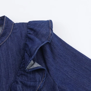 Détail de l'épaule à volants sur une chemise en jean bleu foncé avec surpiqûres contrastées