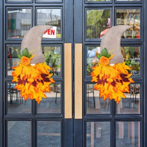 Set of two fall gnome wreaths with burlap hats and autumn maple leaves on a glass door