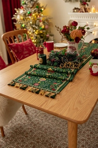 Detailed view of green Christmas table runner with tassels and festive holly motifs