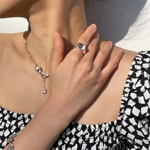 Silver chain necklace with square pendant and zircon ring worn on checkered fabric background