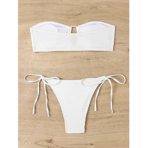 Flat lay of a white textured bandeau bikini set with tie-side bottoms on a wood background