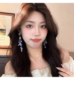 Close-up of elegant purple floral drop earrings with pearls and tassels on model