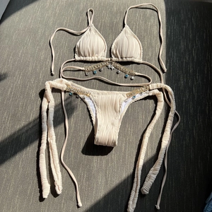 Detail of beige bikini with textured fabric and gold chain links with blue gems