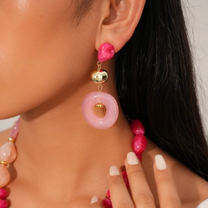 Close-up of pink acrylic resin dangle earrings with gold metal sphere and ring details