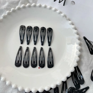Detailed view of ten glossy black teardrop metal BB hair clips on a ceramic plate