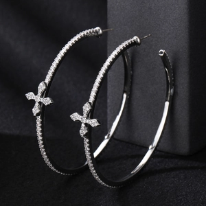 Elegant silver hoop earrings with sparkling zircon cross pendants on a dark box