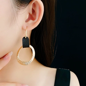 Close-up of golden textured hoop earring with black leather pendant on female model