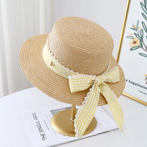 Detail of beige straw hat with plaid lace bow and golden V-shaped metal logo