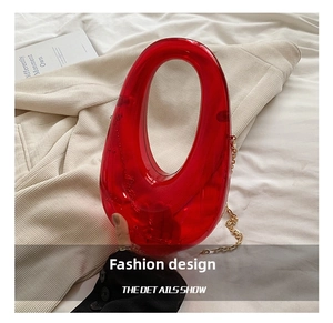 Detail of red transparent acrylic clutch with golden metal chain on knit fabric