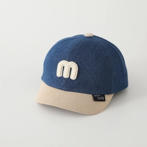 Dettaglio cappello bambino in denim blu con visiera in pile beige e lettera M in rilievo