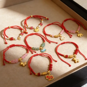 Detail of red woven bracelets featuring gold lucky charms and colorful glass beads