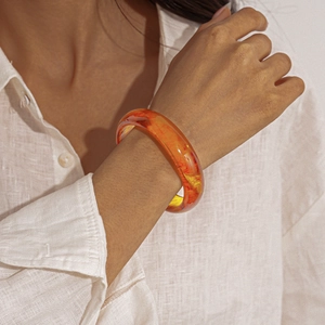 Detail of amber resin round bangle on wrist showing natural red vein textures