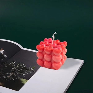 Detailansicht der rosa 3D-Herz-Würfelkerze auf einer Zeitschrift mit grünem Hintergrund