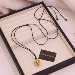 Creative gold pinecone pendant necklace with adjustable black cord on beige velvet box