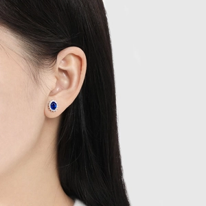Elegant oval sapphire blue stud earrings with white halo stones on female model