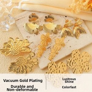 Detail of gold-plated ginkgo leaf and flower earrings on a textured stone display