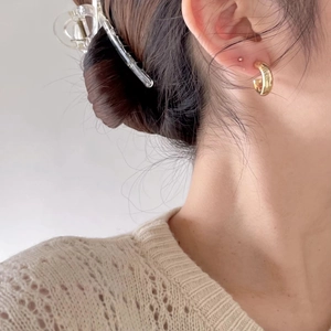 Close-up of elegant gold C-shaped metal earrings worn by a model on a neutral background