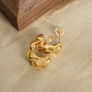 Modern twisted gold-plated hoop earrings with a polished finish on silk background