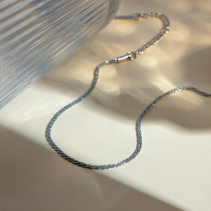 Detail of silver plated snake chain anklet with extension link on textured background