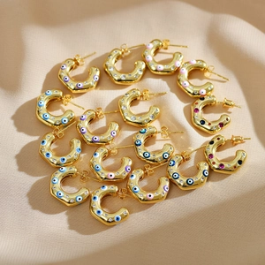 Detailed shot of C-shaped gold earrings with colorful evil eye enamel and zirconia