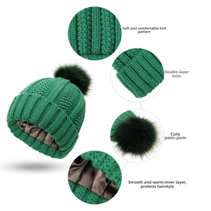 Detail view of green knit beanie with satin lining for hair protection and faux fur pom