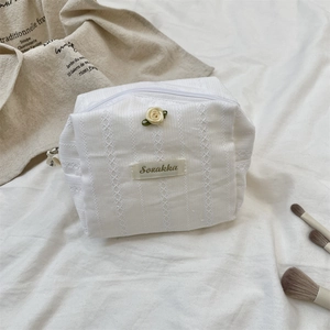 Detail of white floral makeup bag with textured embroidery and decorative 3D rose accent