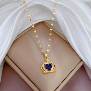 Close-up of golden crown necklace with blue gem and diamonds on white silk