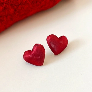Macro di orecchini a lobo a cuore rossi con texture spazzolata su una superficie bianca
