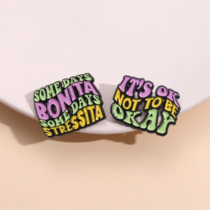 Two enamel pins with English slogans on white pedestal with a soft beige backdrop