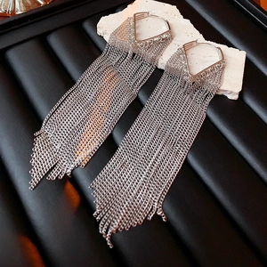Detail shot of silver tassel earrings with triangle studs on a white textured rock