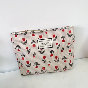 Close-up of beige corduroy pouch featuring red tulip patterns and stitched fabric label