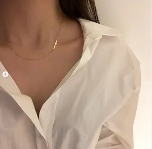 Detail shot of a minimalist gold cross choker necklace worn over a white shirt