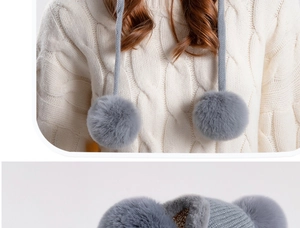 Detail of white cable knit texture with grey faux fur pompom and shiny yarn beanie