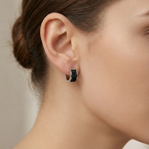 Close-up of silver-toned huggie hoop earrings with black pavé crystals on ear