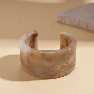 Detail view of wide C-shaped resin bangle with brown marble texture on beige background