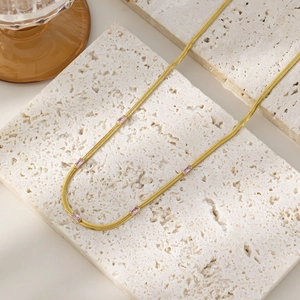 Detailed close-up of gold snake chain necklace featuring five pink zircon stones on marble