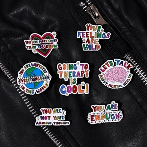 Mental health enamel pins with motivational quotes displayed on a black leather jacket
