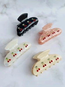 Detail of four acetate hair claws featuring sparkling rhinestone cherry motifs in various colors