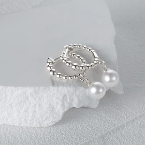 Detail view of elegant S925 sterling silver pearl earrings on white stone surface
