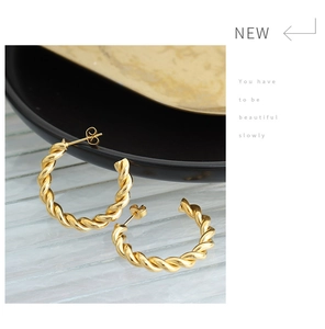 Macro view of gold twisted rope hoop earrings resting on a black porcelain plate