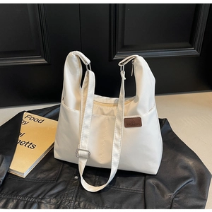 Close-up of cream canvas tote bag showing side pocket and fashion logo on leather jacket