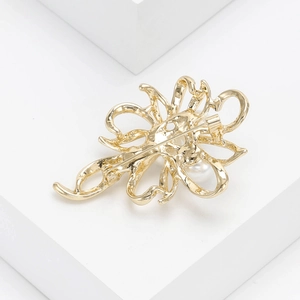 Close-up of elegant gold flower brooch with central pearl detail on white display stand