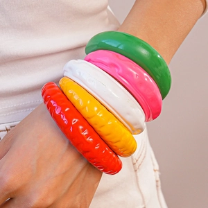 Dettaglio di bracciali colorati in acrilico con design a onde in rosa verde e giallo