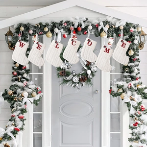 Knitted white Christmas stockings with red embroidered WELCOME letters hanging on a door