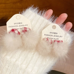 Detail of S925 silver needle earrings with white fluffy pom-poms and red plaid bows