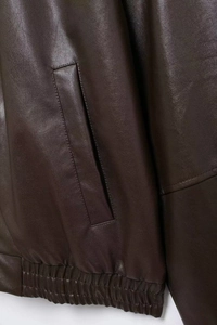 Detail of dark brown faux leather jacket showing pocket stitching and elastic hem