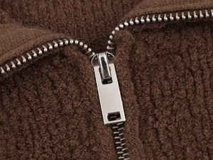Macro shot of polished silver metal zipper on a dark brown textured boucle bomber jacket