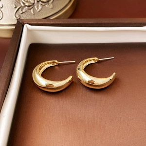 Macro view of gold-tone C-shaped knot earrings with S925 hallmark on silver posts