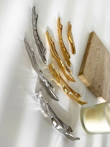 Detailed collection of textured gold and silver irregular wavy metal hair clips on stone