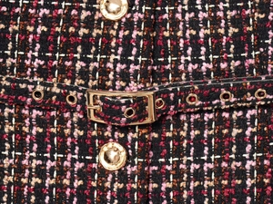 Nahaufnahme des Tweed-Stoffs mit goldenen Knöpfen und Gürtelschnalle im Detail